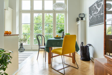 Large shopping bag next to a wooden table with a green tablecloth and a bowl of lemons in a natural kitchen and dining room interior
