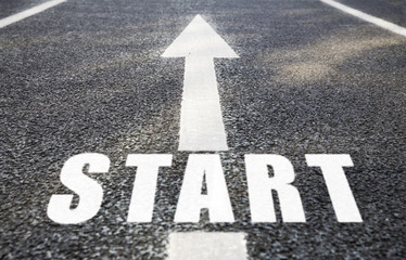 new beginnings, road surface marking and traffic concept - close up of arrow and word start on asphalt
