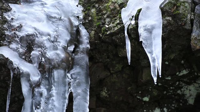 Acqua di ruscello in montagna che  scorre sotto stalattiti di ghiaccio in scioglimento 