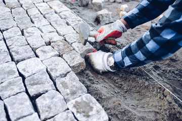 industrial worker installing pavement rocks, cobblestone blocks on road pavement