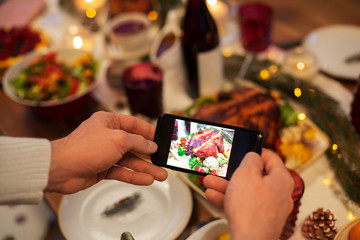 food, technology and holidays concept - close up of male hands photographing roast turkey by smartphone at christmas dinner