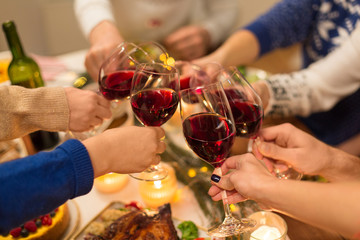 holidays and celebration concept - close up of friends having christmas dinner at home, drinking red wine and clinking glasses