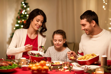holidays, family and celebration concept - happy mother, father and little daughter having christmas dinner at home