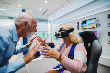 Mature couple in adventure at tech store with virtual reality goggles.