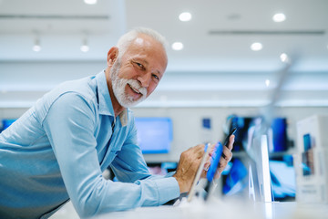 Beautiful senior man portrait at tech store. Looking for a new smart phone.