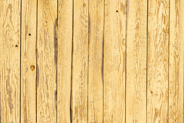 A fragment of a wooden fence. Vertical boards. Yellow old paint