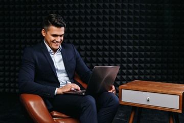 Brunette young male looking for information in computer and smiling against dark background