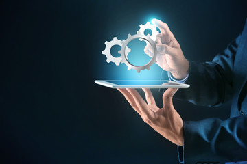 Businessman with tablet PC and digital gearwheels on dark background. Concept of Internet and...