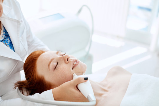 Apparatus Face Treatment In Medical Spa Center, Beautiful Redhead Lady Receiving Electric Facial Peeling Massage. Cosmetological Methods, Apparatus Cosmetology, SPA-procedures Concept.