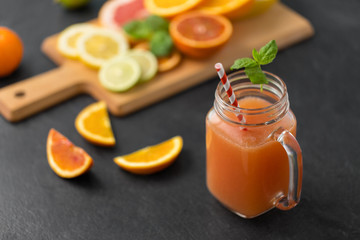food , healthy eating and vegetarian concept - mason jar glass of grapefruit juice with straw and citrus fruits on slate table top