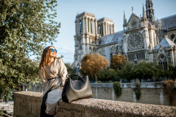 Young woman tourist sitting near the famous Notre Dame cathedral during the morning light traveling...