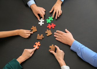 Business team assembling puzzle on dark table