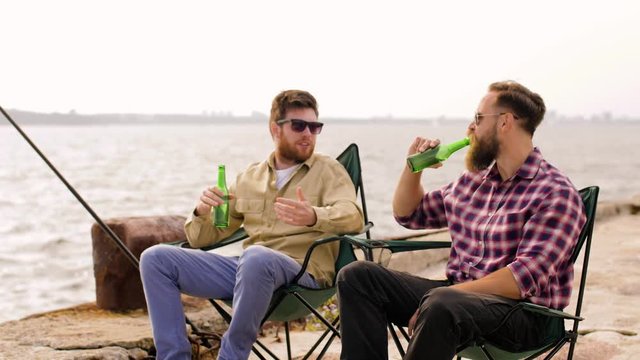 leisure and people concept - happy friends fishing and drinking beer on pier