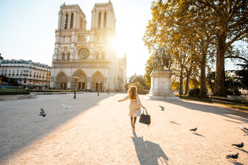 Morning view on the famous Notre-Dame cathedral with woman running on the square dispersing pigeons...