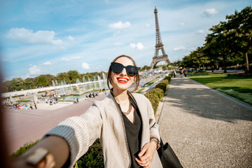 Lifestyle portrait of a young woman walking in front of the famous Eiffel tower during the sunny...
