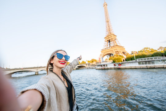 Young woman tourist making selfie photo with Eiffel tower on the background from the boat during the sunset in Paris