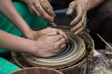hands of a potter, helping to a boy create an earthen jar on the circle