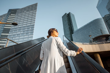 Stylish businesswoman in white suit going up on the escalator at the business centre outdoors with...
