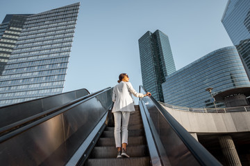 Stylish businesswoman in white suit going up on the escalator at the business centre outdoors with skyscrapers on the background in Paris - Powered by Adobe