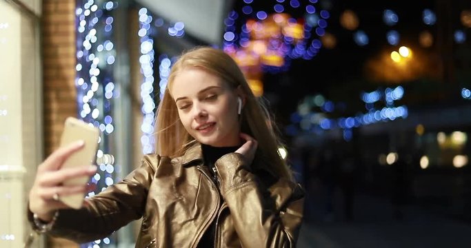 Selfie time, Young funky blogger is making photo for her social networks page. Young happy woman taking selfie at night. atmosphere and a beautiful smiling girl. wireless earphones