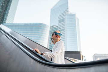 Stylish businesswoman in white suit going up on the escalator at the business centre outdoors with...