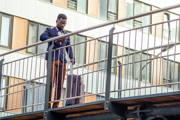 Full length portrait of successful and well dressed African american businessman walking for flight at airport with wheeled bag large suitcase on wheels
