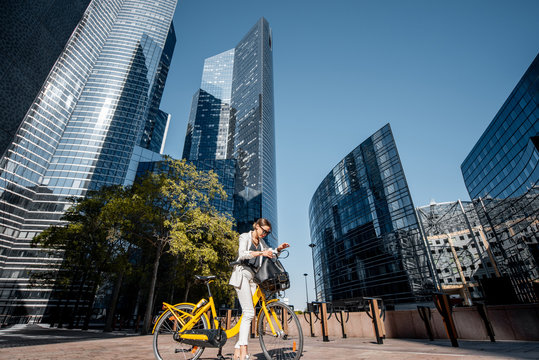 View on the financial district with business woman in white suit standing with bicycle outdoors