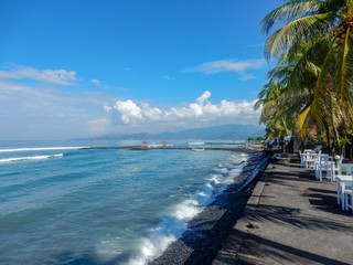 Balinese beach with black sand, palm trees and beach cafe tables