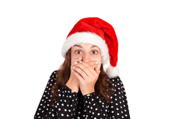 Girl scared and closes the mouth with her hands. emotional girl in santa claus christmas hat isolated on white background. holiday concept