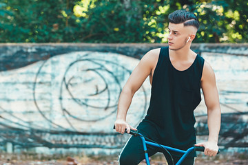 lifestyle, transport and people concept - young man with bluetooth headphones posing on bicycle on city street