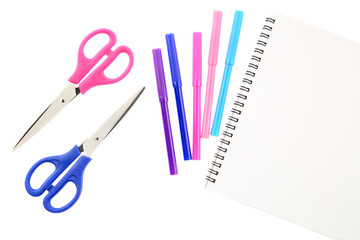 Two scissors, five felt tip pens in pink, blue and purple colors and blank sketchbook, isolated on white background. Space for text on the pad sheet. Art and creativity concept