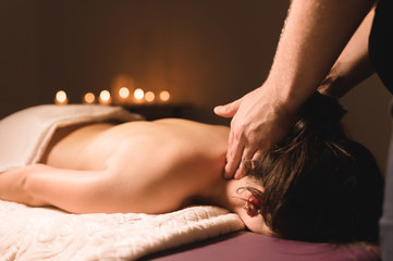 Men's hands make a therapeutic neck massage for a girl lying on a massage couch in a massage spa...