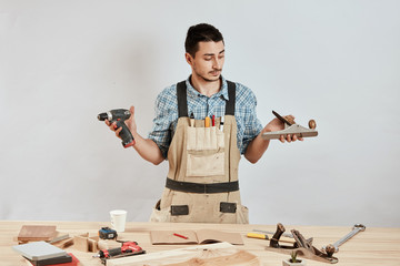 Pessimistic, unconvinced, annoyed cabinetmaker at the table with plane and drill. Puzzled craftsman...