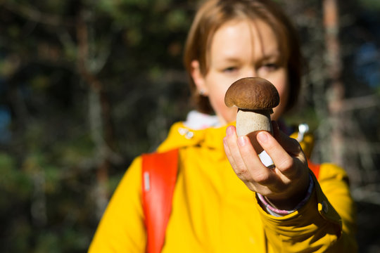 Girl in a yellow jacket with a backpack and a basket holds in her hand a porcini mushroom at the forest background