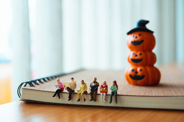 Miniature people sitting on book with ghost pumpkin background using as family and halloween concept