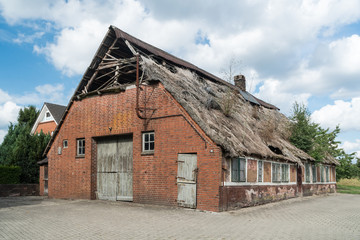 Fototapeta na wymiar Bauernhaus mit Scheune und einem beschädigten Reetdach