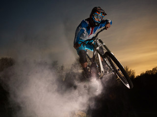 Downhill cycling. Man jump on a mountain bike with dust. Extreme sport.
