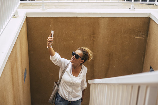 Middle Age Caucasian Beautiful Lady With Blonde Curly Hair Looooking For Wifi Internet Signal On The Phone Outdoor. Modern People Use Technology And Stay Always Connected Like Addicted