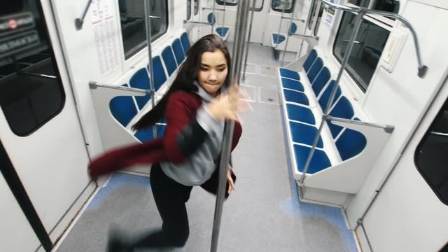 Young woman dancing pole dance in moving train, jumps on the pole and hanging on it