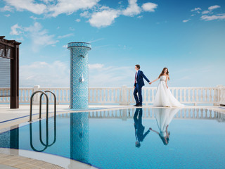 Bride and groom near the swimming pool. Honeymoon wedding the young couple. A man in a suit holding...