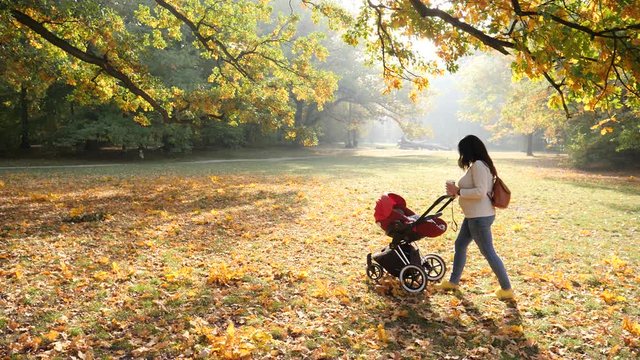 Young mother woman with baby in stroller walking beautiful autumn park drinking coffee cup