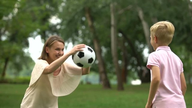 Boy playing soccer with mom in park, happy family weekend, healthy lifestyle