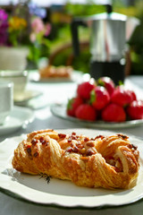 Sunny Sunday morning breakfast served outdoor in summer garden with fresh baked pastry and strawberry