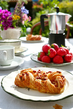 Sunny Sunday morning breakfast served outdoor in summer garden with fresh baked pastry and strawberry