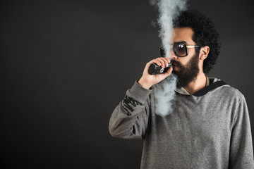 Vaping man holding a mod. A cloud of vapor. Black background. Vaping an electronic cigarette with a lot of smoke. Vape concept