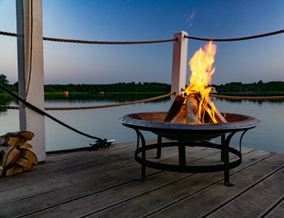 Feuer in einer Feuerschale am Abend am See - obrazy, fototapety, plakaty