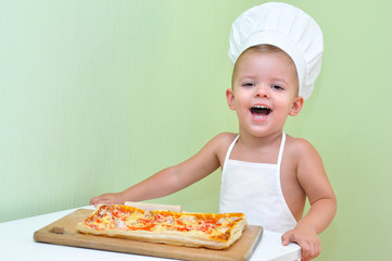 A little boy baker and pizza maker in a white chef's cap and apron is smiling because he cooked delicious and beautiful puff pastry pizza.
