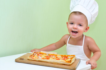 A little boy baker and pizza maker in a white chef's cap and apron is smiling because he cooked delicious and beautiful puff pastry pizza.
