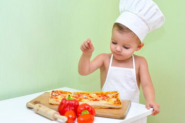 A little boy baker and pizza maker in a white chef's cap and apron is smiling because he cooked delicious and beautiful puff pastry pizza.
