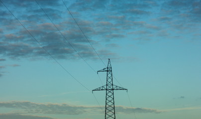 Top of electricity pylon and power lines in front of calm blue evening sky and clouds